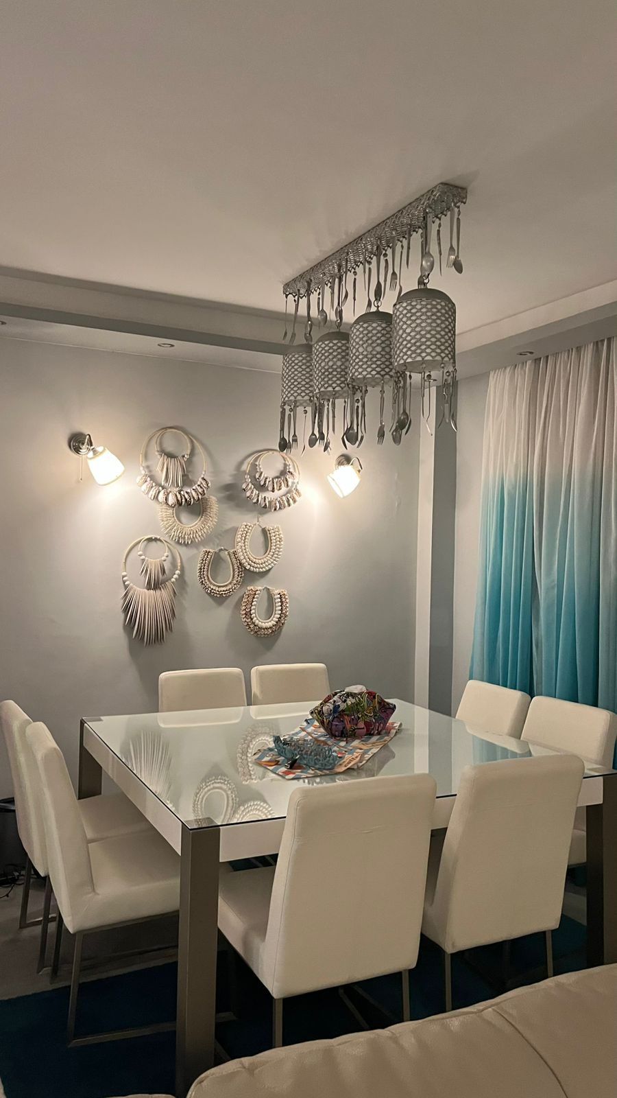 Dining room with white table, shell wall decor, cutlery chandelier and ombre turquoise curtains