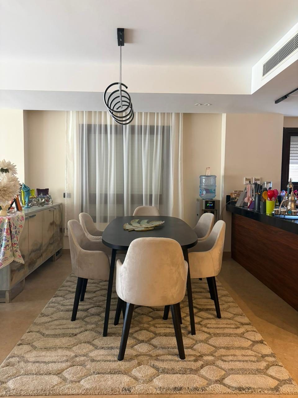 Dining area with oval black table, upholstered chairs and spiral pendant light
