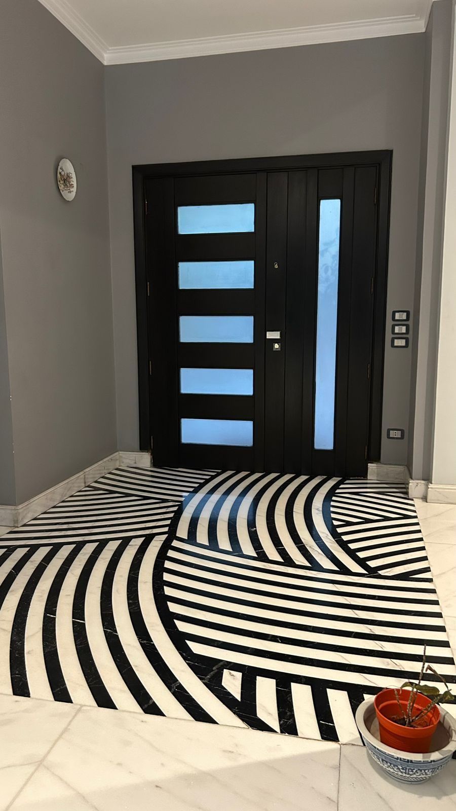 Black entrance door with glass inserts over a striped marble inlay
