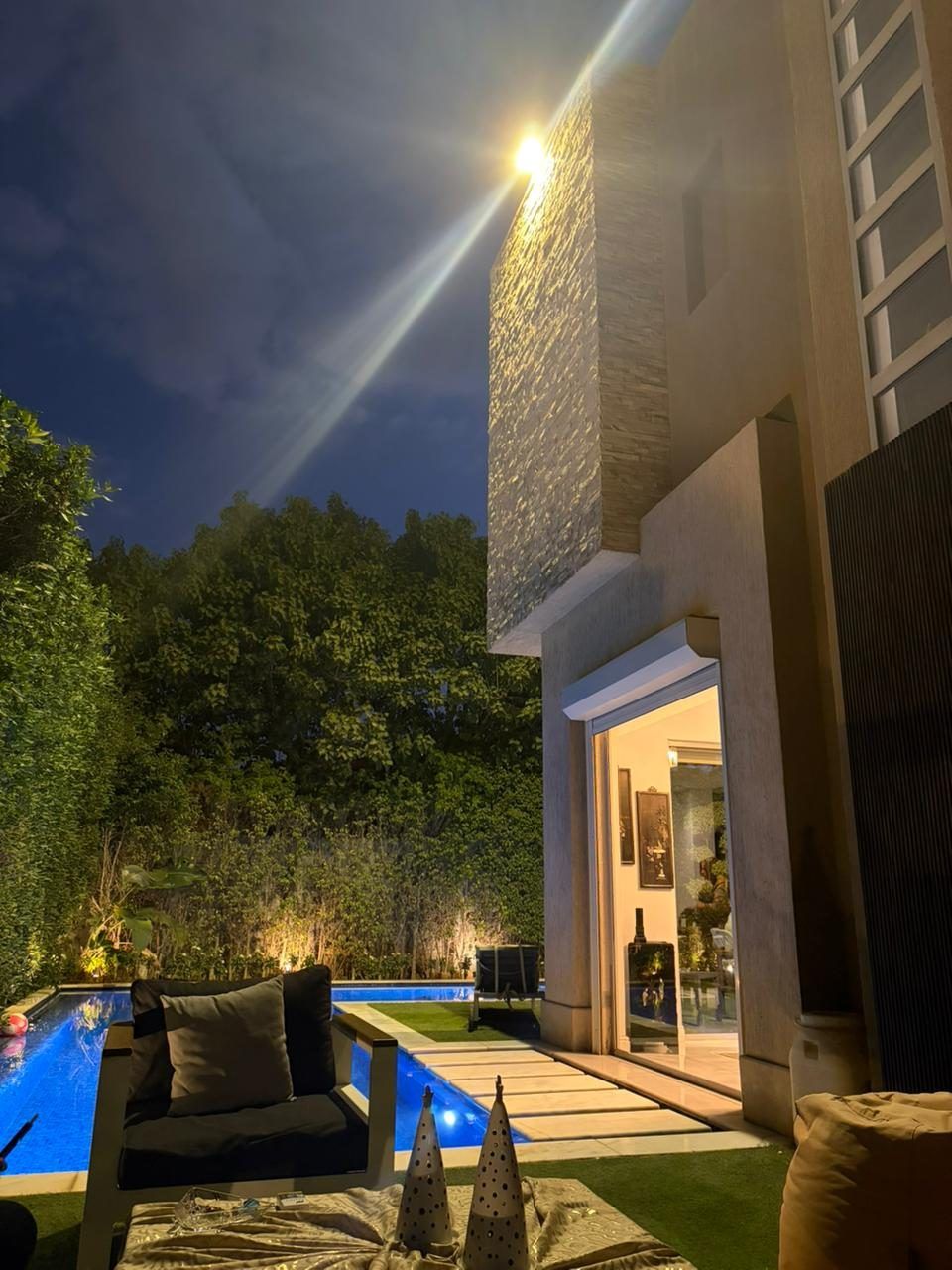 Garden terrace and pool at night with stone-clad facade and warm uplighting