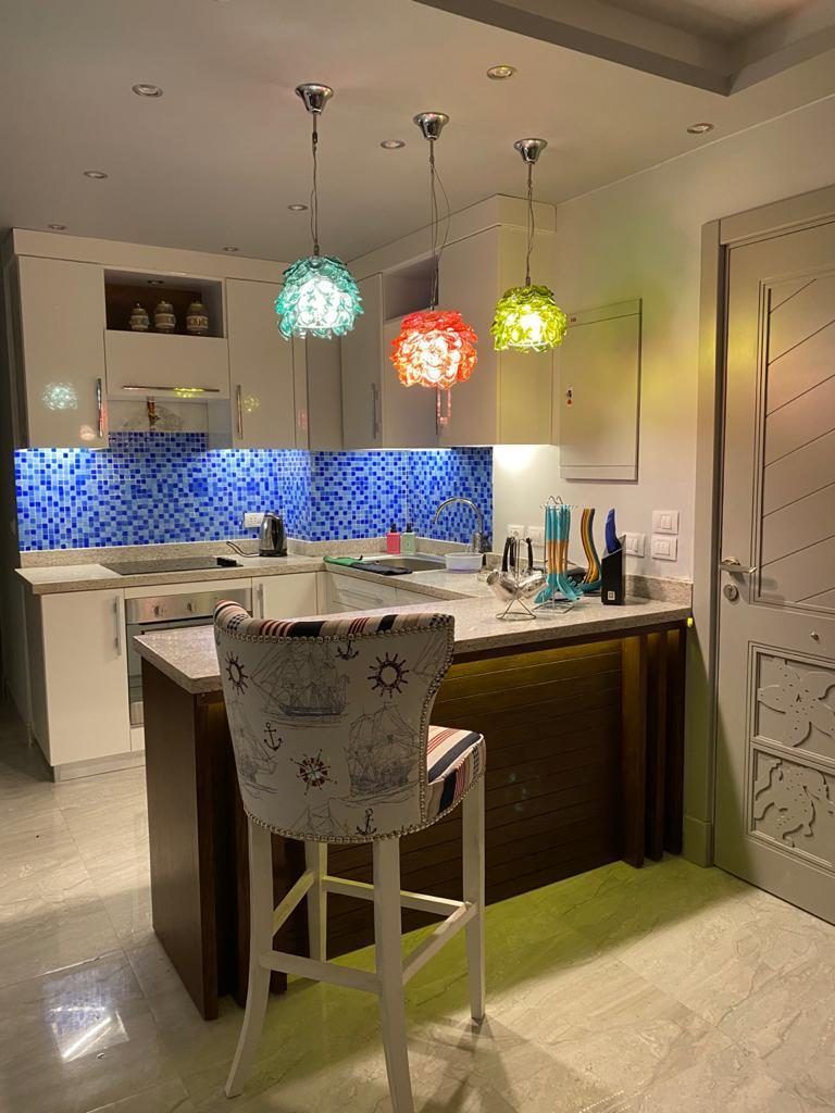 White kitchen with blue glass mosaic backsplash, granite breakfast bar and colourful glass pendant lights