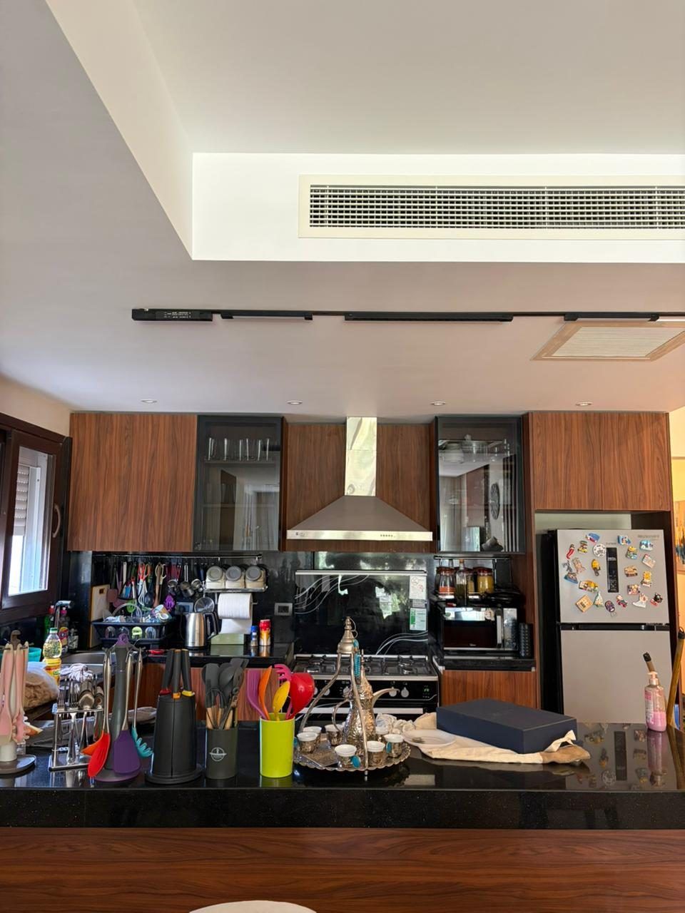 Walnut and black kitchen with stainless hood under a cove-lit bulkhead