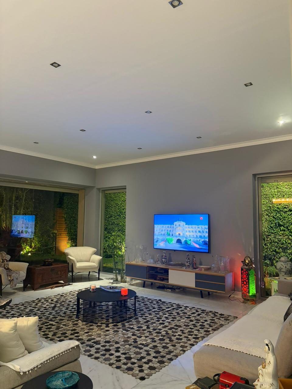Living room with patterned rug, cove lighting and green garden views on two sides