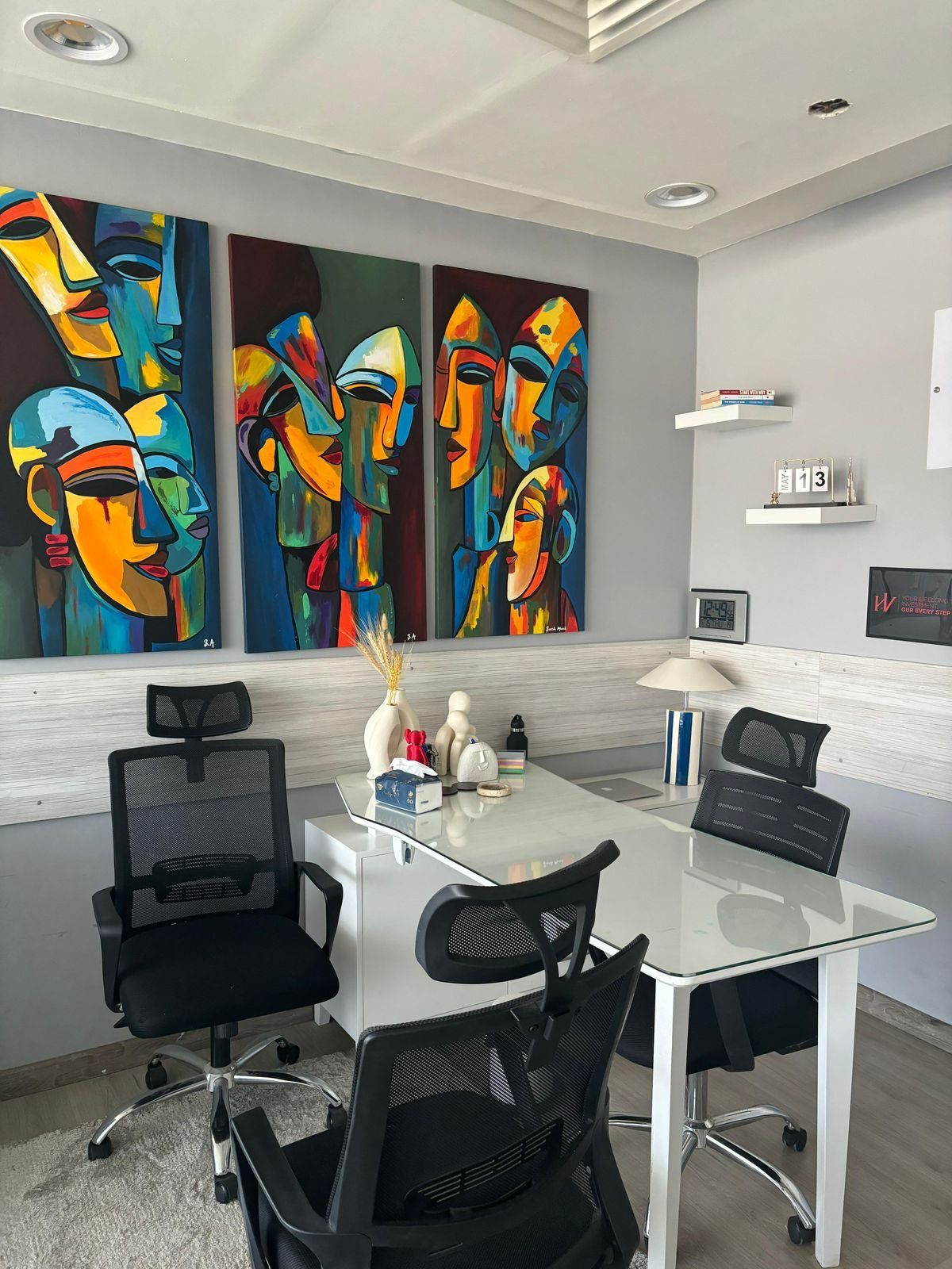 Office with grey walls, whitewashed timber wainscot, glass desk and a triptych of colourful abstract paintings