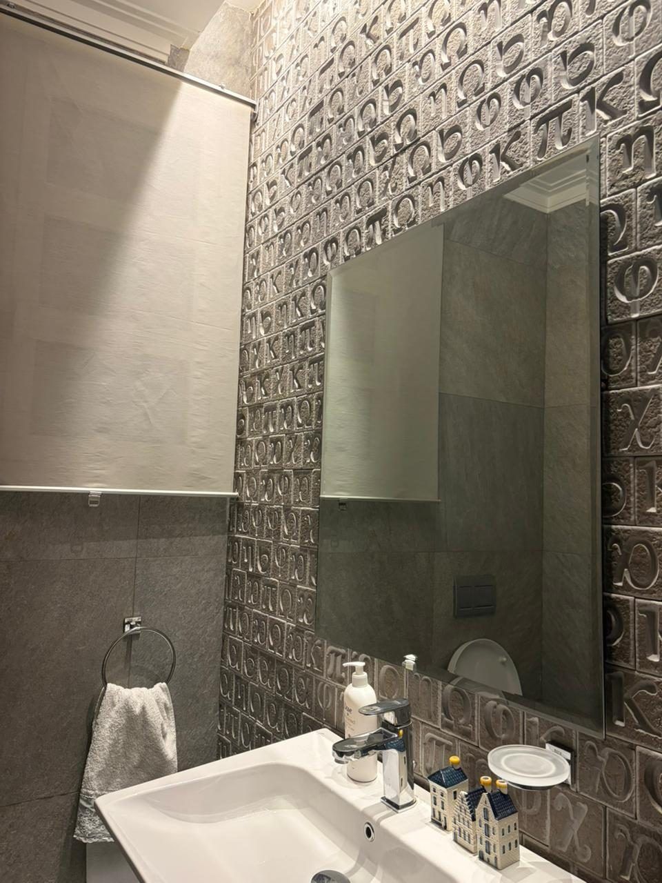 Powder room with embossed metallic wall tiles and frameless mirror